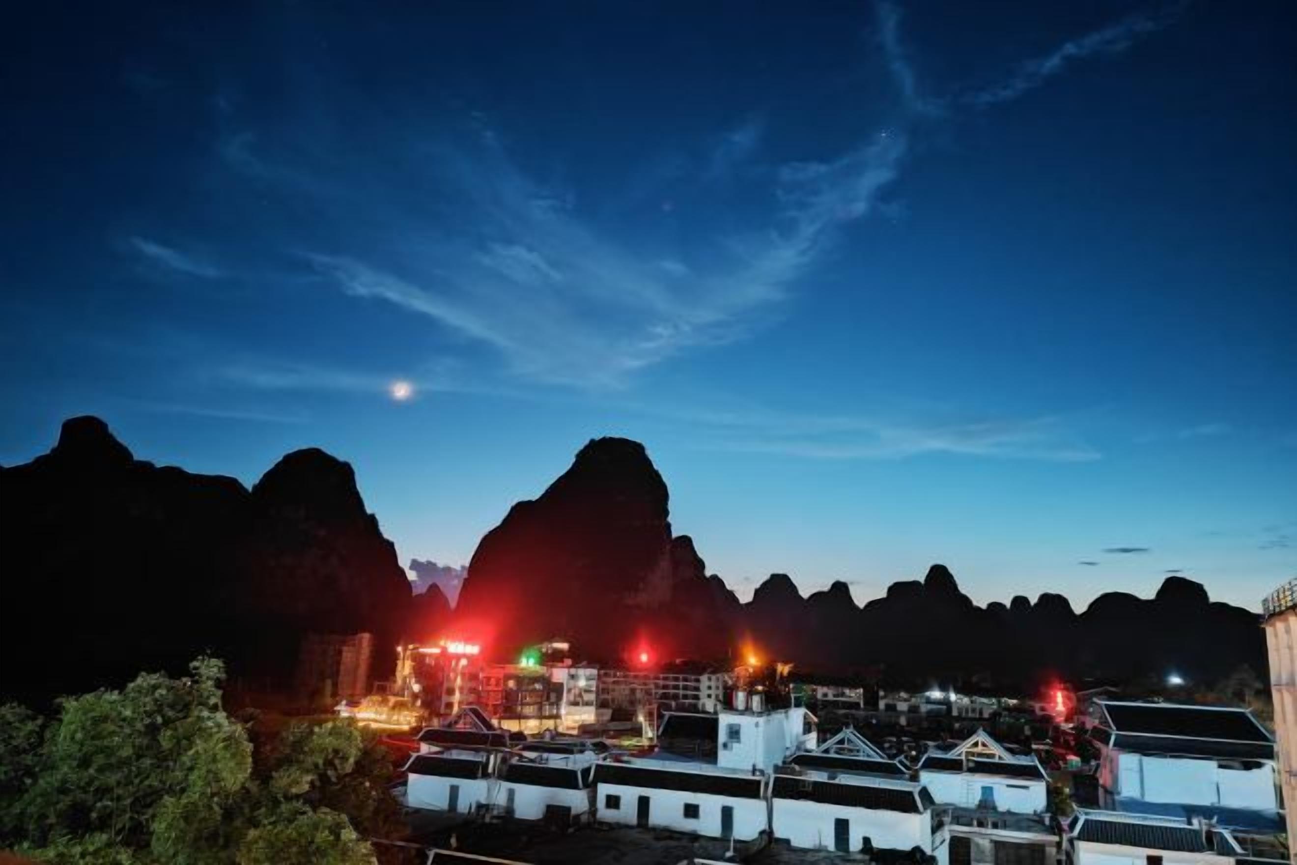 A night view of a coastal town with buildings and a mountain backdrop.