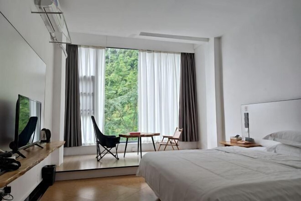 Une chambre d’hôtel comprenant un lit, un bureau avec un ordinateur, une chaise, une petite table et une fenêtre avec des rideaux.