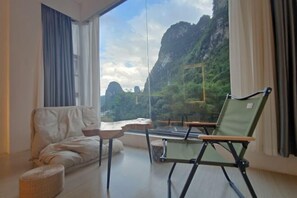 A room with a large window, a sofa, a chair, and a small table. - Daxin Mingxuan Qianzhuyuan Hotel (Daxin)