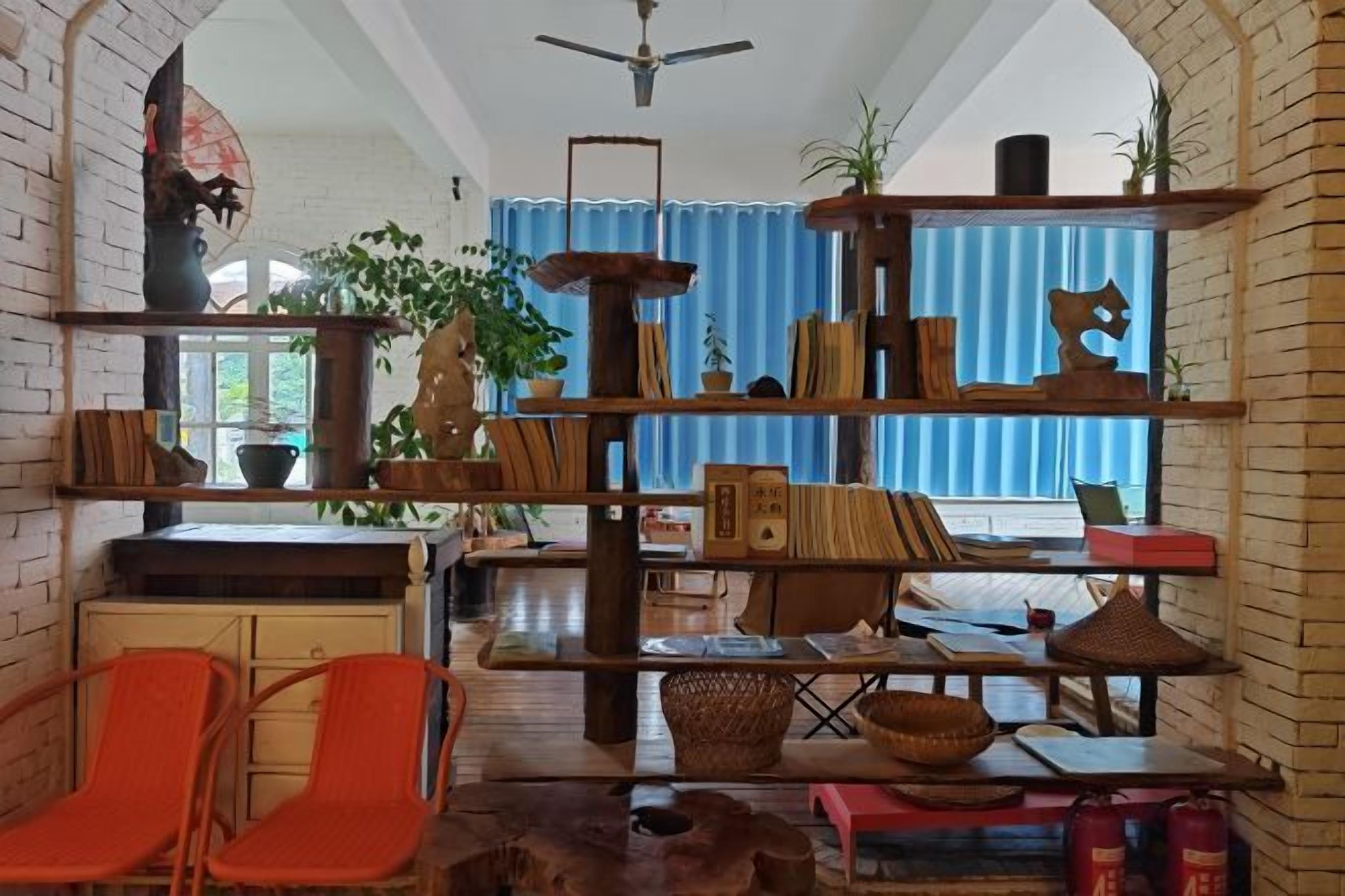 A room with a brick wall, a wooden bookshelf, a dining table with chairs, and a window with blue curtains.