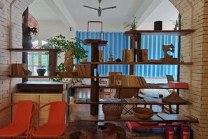 A room with a brick wall, a wooden bookshelf, a dining table with chairs, and a window with blue curtains. - Daxin Mingxuan Qianzhuyuan Hotel (Daxin)