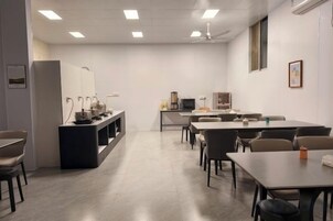 Un salón de conferencias con una mesa larga, sillas, una kitchenette y un televisor.