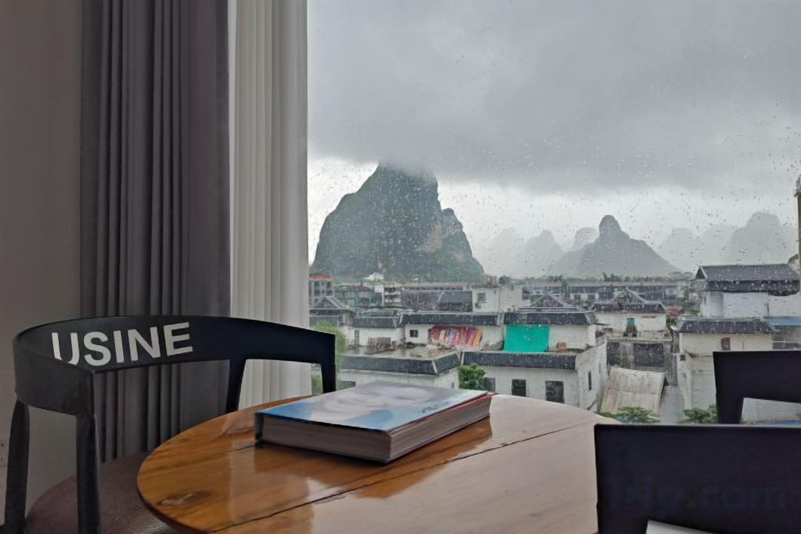 Una habitación con vistas a una montaña, una silla con la etiqueta 'USINE' y una mesa con un libro.
