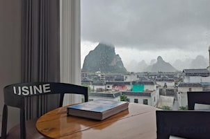Una habitación con vistas a una montaña, una silla con la etiqueta 'USINE' y una mesa con un libro.