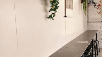 Una larga mesa oscura con sillas, una pared blanca con una planta vertical, y una obra de arte colgada en la pared.