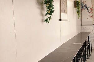 Una larga mesa oscura con sillas, una pared blanca con una planta vertical, y una obra de arte colgada en la pared.