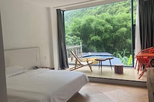 Un dormitorio con una cama grande, un balcón con mesa y sillas, y vistas a zonas verdes.
