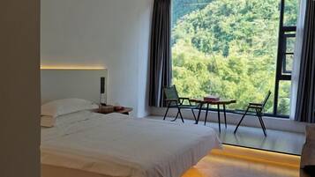 A bedroom with a bed, a nightstand, a window with curtains, and a view of a forest.