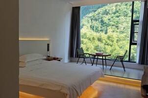 A bedroom with a bed, a nightstand, a window with curtains, and a view of a forest.