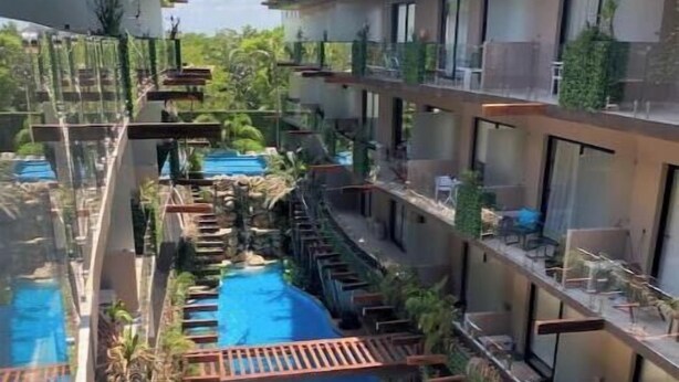 A modern hotel with a central swimming pool, balconies with plants, and a clear view of the surrounding area. - Dep 1 room, green terrace and view (Tulum)
