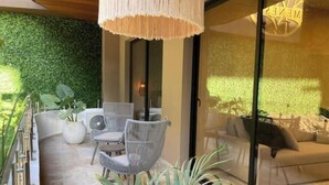 A modern outdoor seating area with wicker chairs and a table, a glass door leading to a living room, and a green wall. - Dep 1 room, green terrace and view (Tulum)