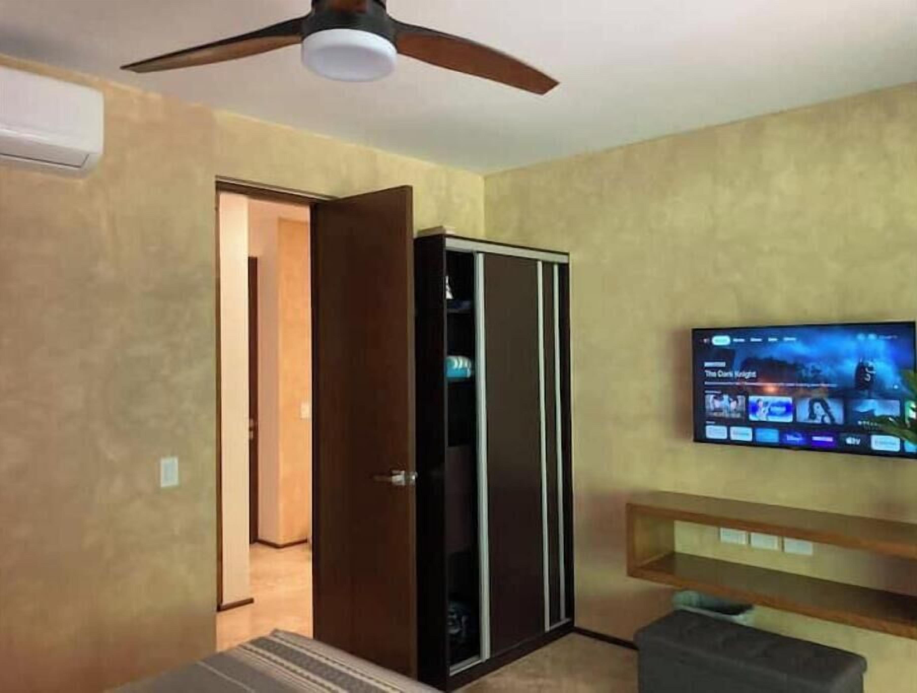 A room with a ceiling fan, a TV mounted on the wall, and a sliding door closet.