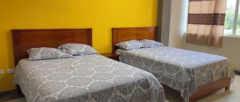 A room with two wooden beds, each with patterned bedding, a yellow wall, and a framed picture above the beds.