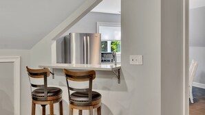 A kitchen with a white countertop, stainless steel refrigerator, and two wooden chairs with metal accents.