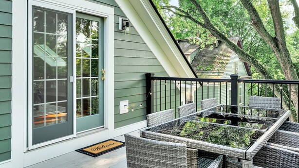 A green house with a sliding glass door, a small outdoor seating area with wicker furniture, and a black railing.