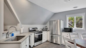 A modern kitchen with stainless steel appliances, a large island with a sink, and a dining area with white chairs.