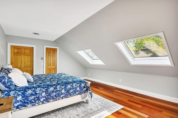 Un dormitorio con cama, puertas de madera, tragaluces y vistas al exterior con vegetación.