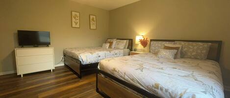 A bedroom with two beds, a TV on a dresser, and a ceiling fan.