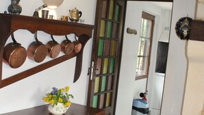 Un pasillo con un estante de madera que alberga varias ollas de cobre, una pequeña mesa con un jarrón de flores y un suelo de baldosas.