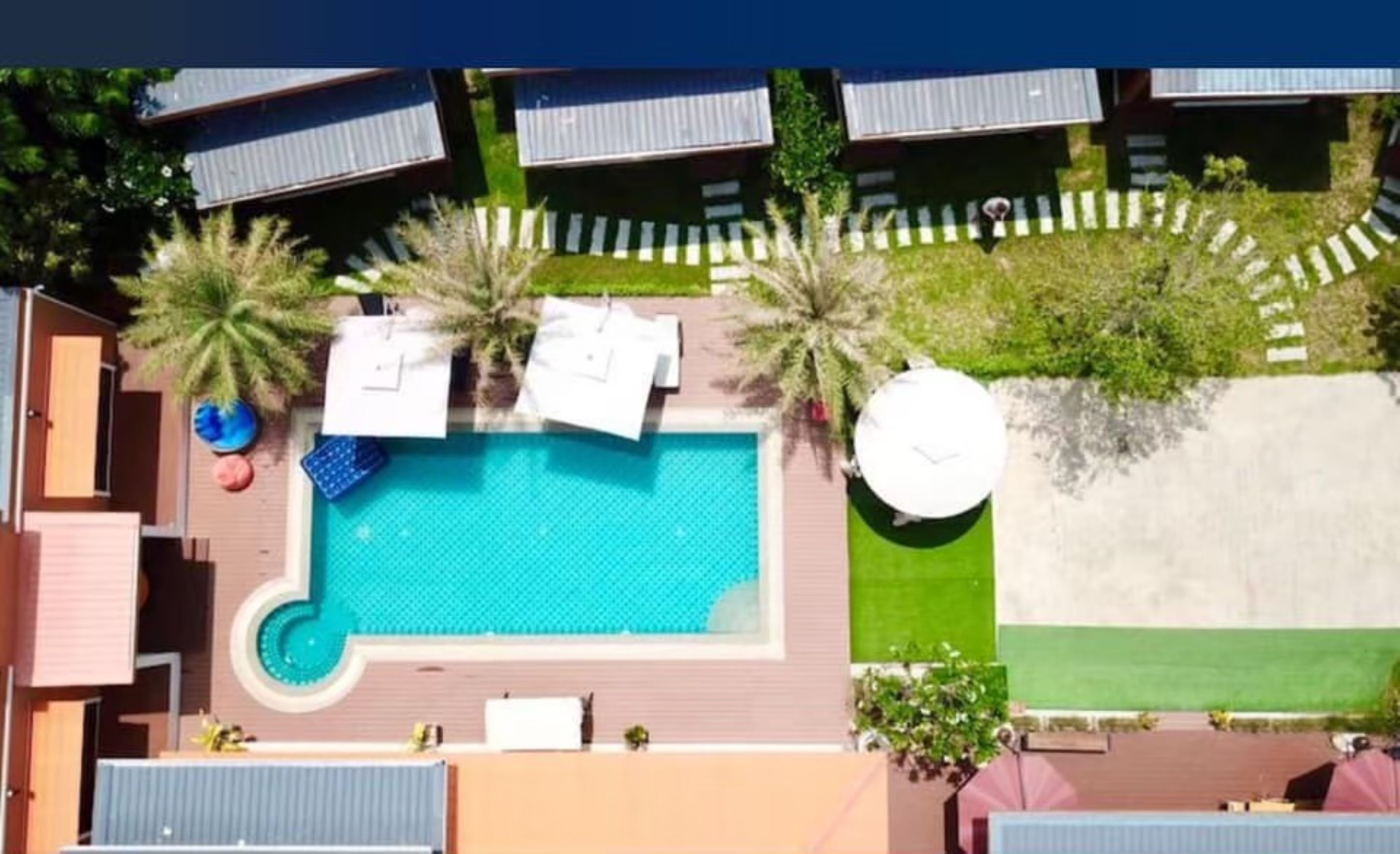 Luchtfoto van een resort met een centraal gelegen zwembad, meerdere bungalows en een verzorgd gazon.