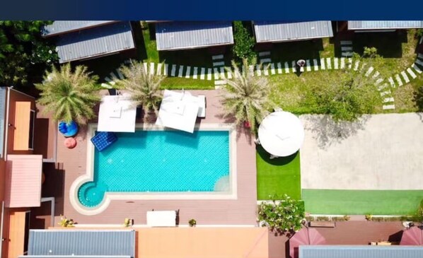 Vista aérea de un complejo turístico con piscina central, varias cabañas tipo bungalow y un césped bien cuidado.