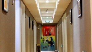 En hotelgang med tæppe på gulvet, billeder i rammer på væggene og en farverig dør i enden.