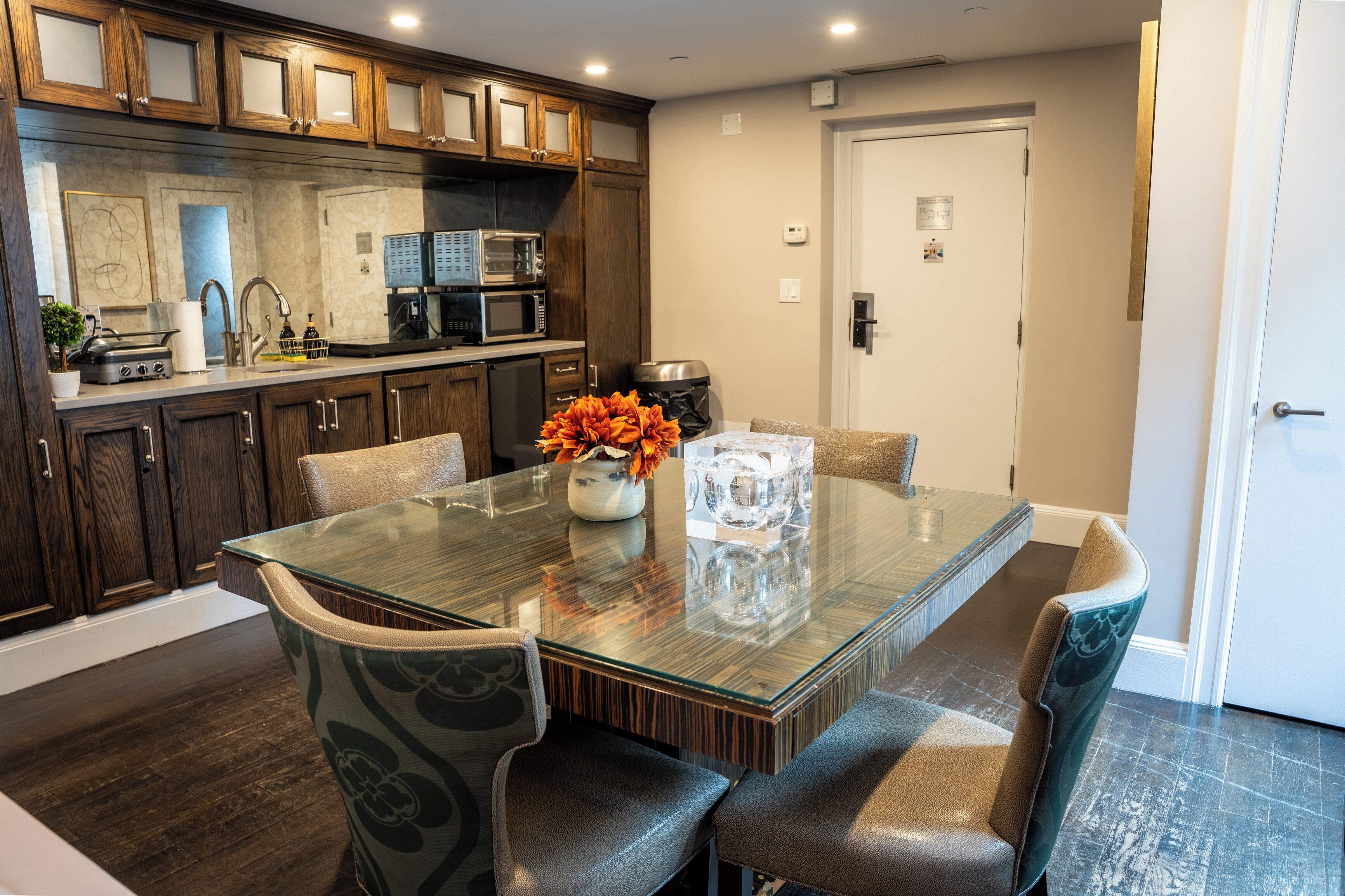 A modern kitchen with dark wooden cabinets, a glass-top dining table, and a vase with orange flowers.