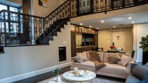 Un amplio espacio de estar con una escalera, un sofá, una mesa de centro y una cocina al fondo.