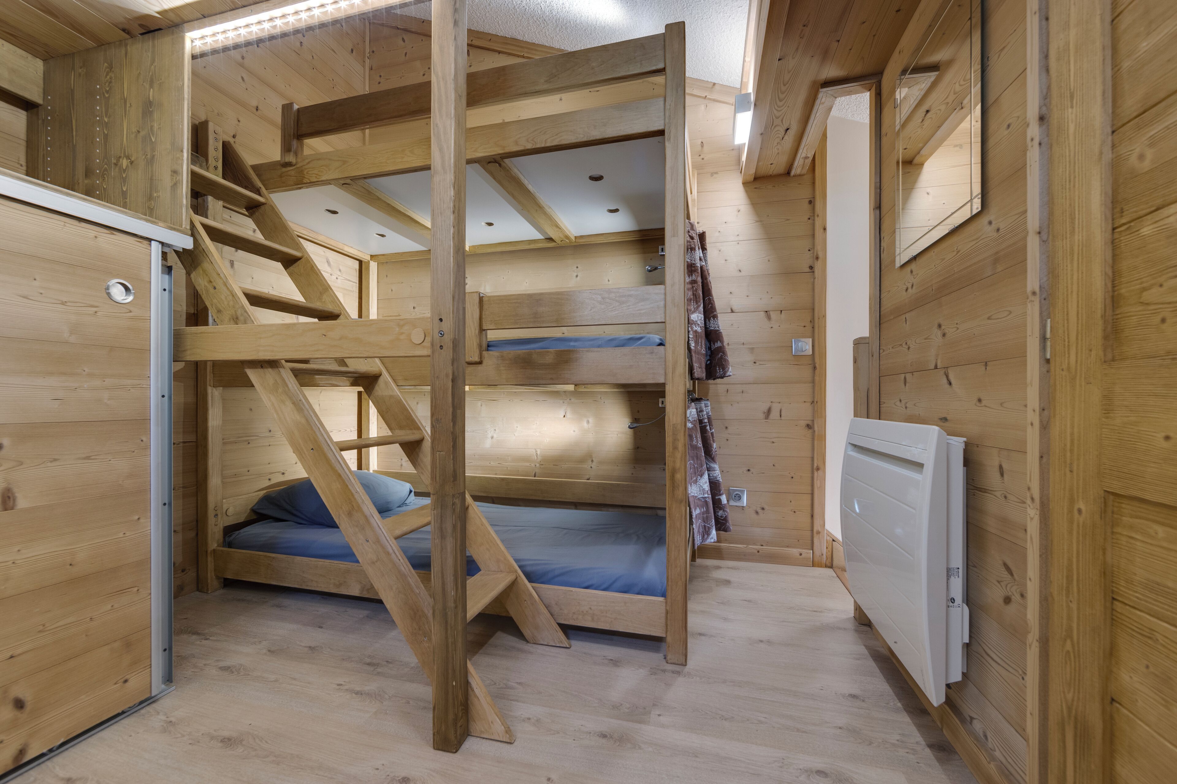 A wooden interior with a bunk bed, a staircase, and a radiator.