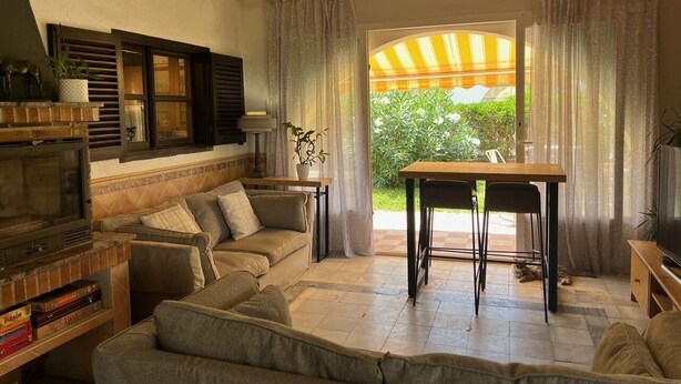 Una sala de estar con un sofá, un televisor, una mesa y una ventana con cortinas.