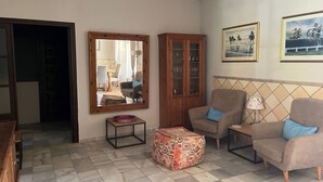 Una sala de estar con un sofá, sillones, una mesa de centro, un reposapiés estampado, un aparador y cuadros enmarcados en la pared.