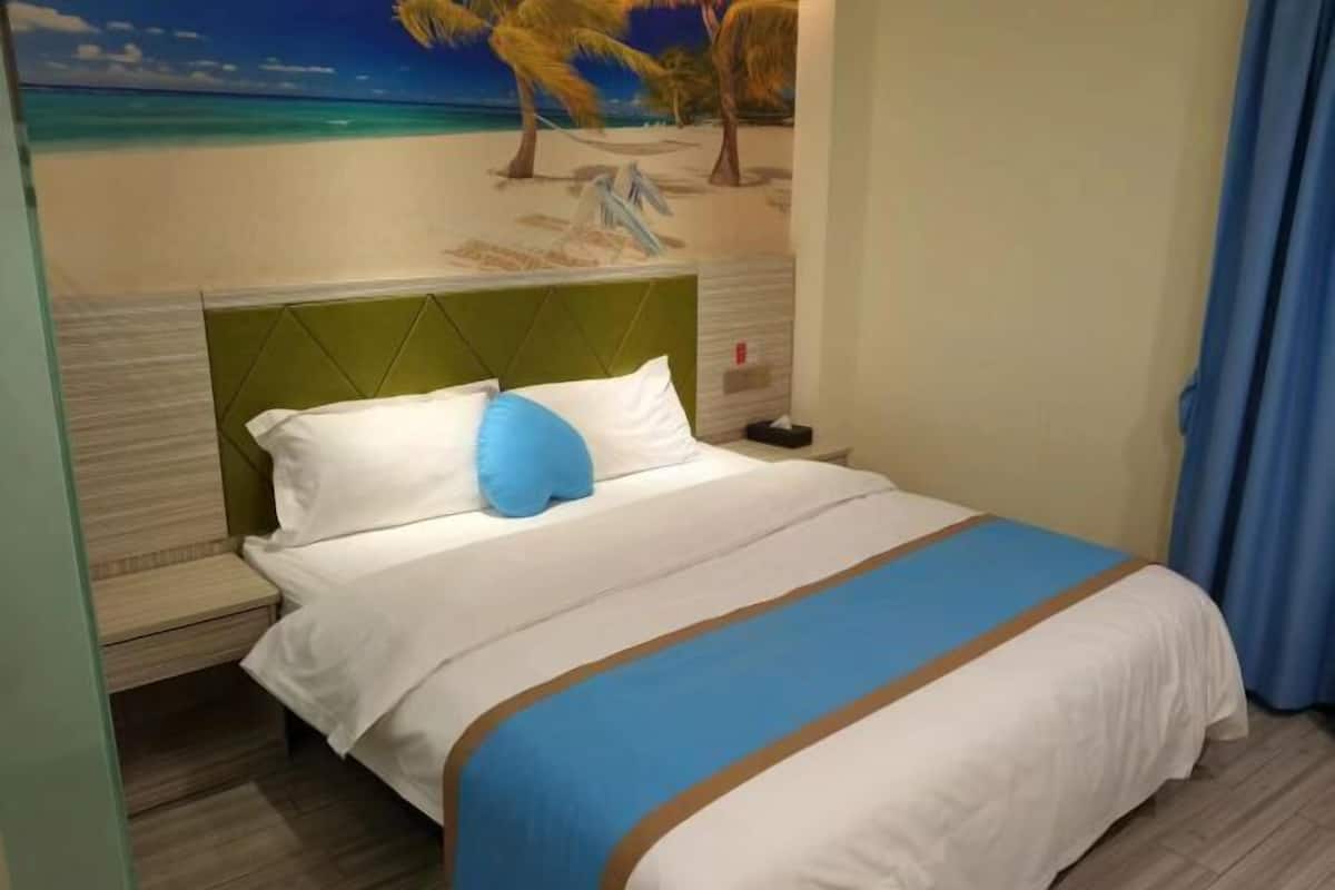 A hotel room with a bed, a headboard, a nightstand, a wall mural, and a window with curtains.