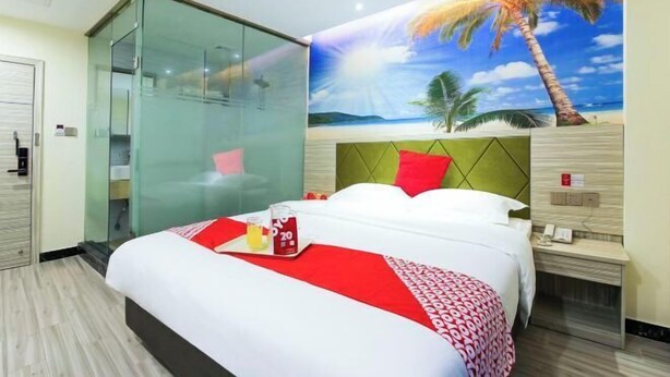 Una camera d'albergo con un letto, una parete divisoria in vetro, un affresco raffigurante una spiaggia e un comodino con il telefono.