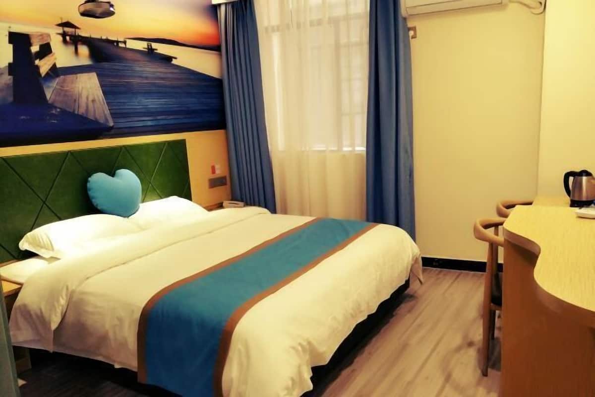 A hotel room with a bed, a desk, a view of a pier, and a painting on the wall.
