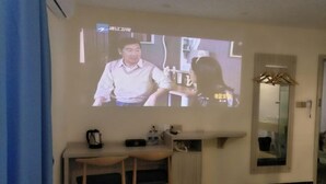 Una stanza con una televisione a parete, una piccola scrivania con due sedie, uno specchio e un armadio.