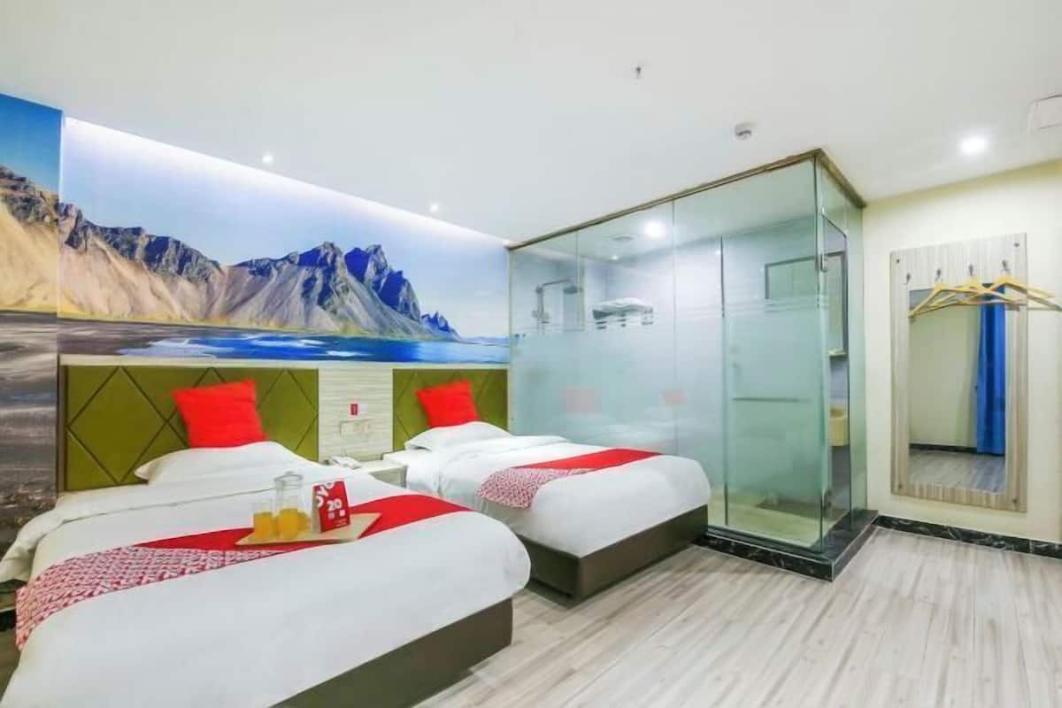 A hotel room with two beds, a glass-enclosed shower, and a mural of a mountainous landscape.