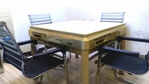 Un tavolino piccolo e quadrato con piano chiaro e quattro sedie nere dalla struttura in metallo.