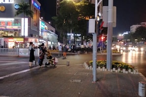 A nighttime urban street scene with pedestrians, a stroller, and illuminated storefronts.