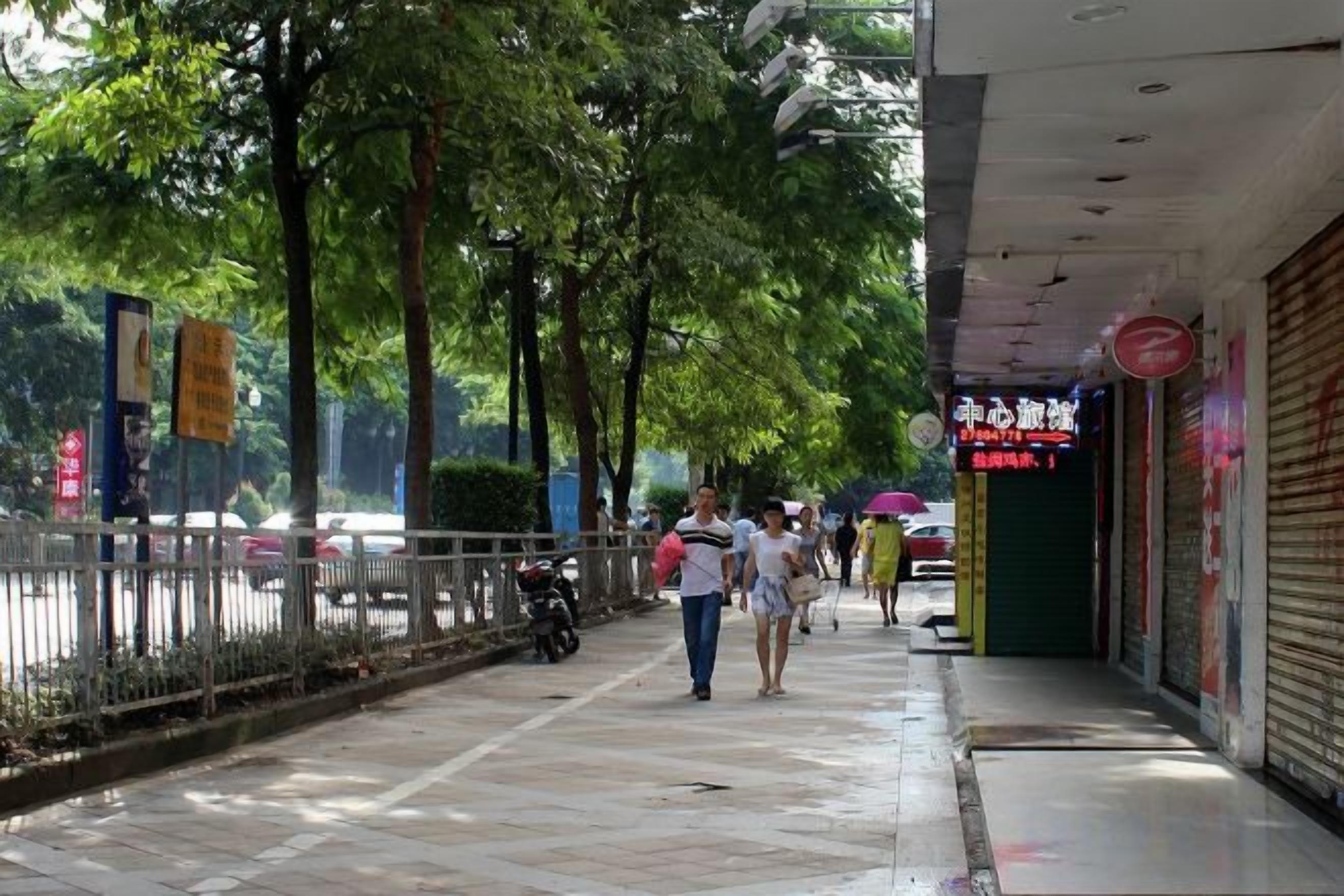 Une promenade piétonne bordée d’arbres et de boutiques, dont certaines ont leurs volets fermés.