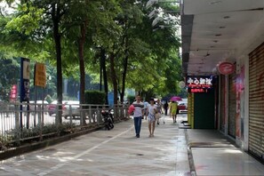 A pedestrian walkway lined with trees and storefronts, some with closed shutters. - Shenzhen Center Theme Hotel (Shenzhen)