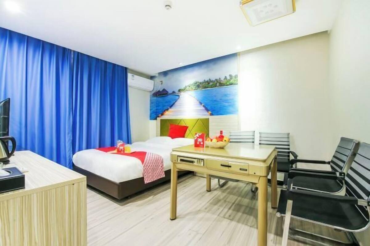 A hotel room with a bed, a desk, a chair, a table, and a mural of a pier leading to a body of water.