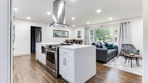 Una cucina moderna con mobili bianchi, piano cottura integrato e cappa aspirante in acciaio inossidabile.