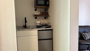 Eine kompakte Küche mit Mikrowelle, Spüle und Geschirrspüler. Darüber befindet sich ein Holzregal.