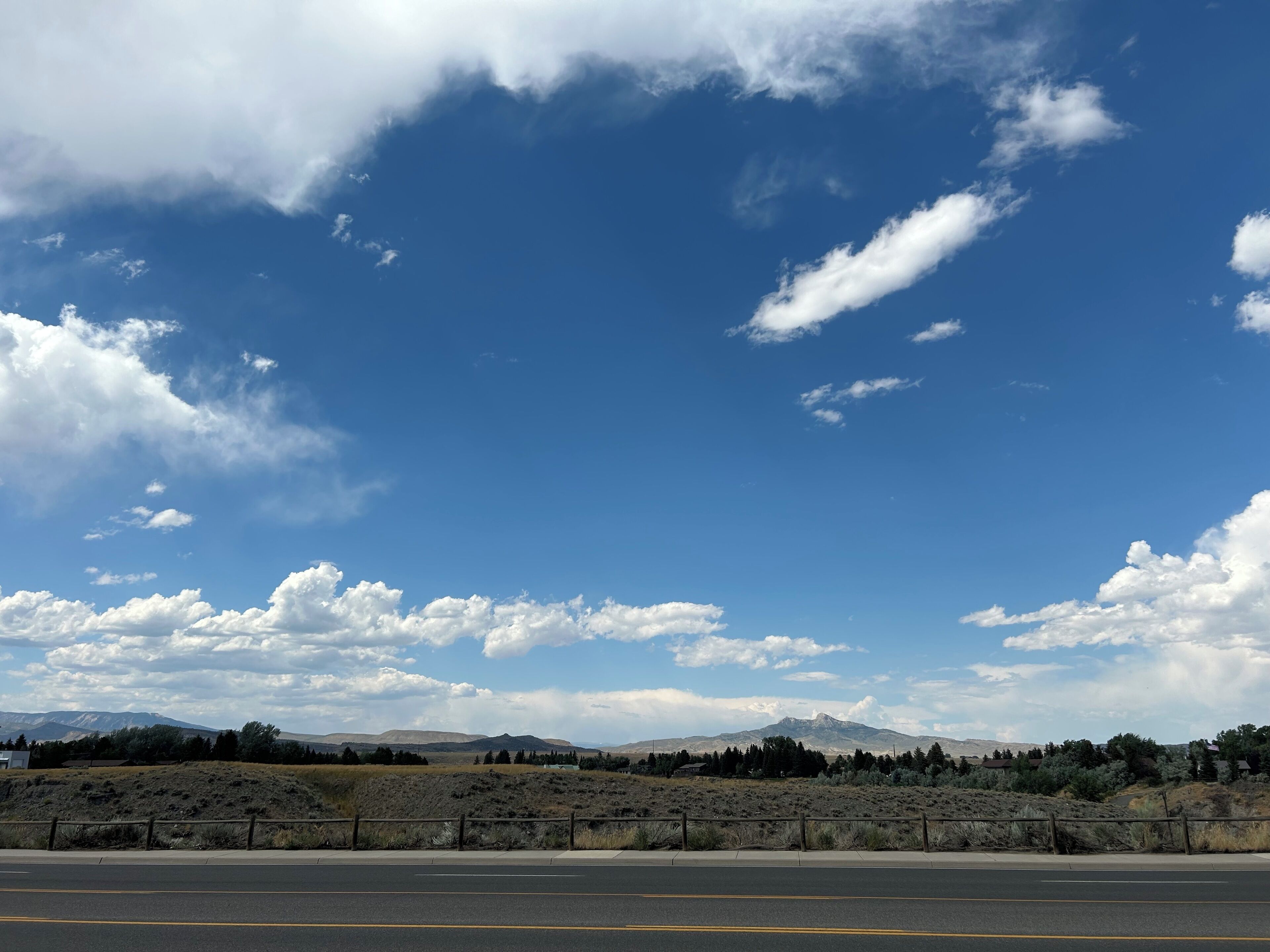 Una carretera con barandilla y un cielo azul despejado con nubes dispersas.