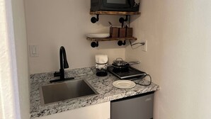 Eine kompakte Küche mit Granit-Arbeitsplatte, Spüle aus Edelstahl, Mikrowelle, kleinem Herd und Geschirrgestell.