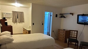 A hotel room with two beds, a wooden dresser, a television, and a bathroom visible through an open door.