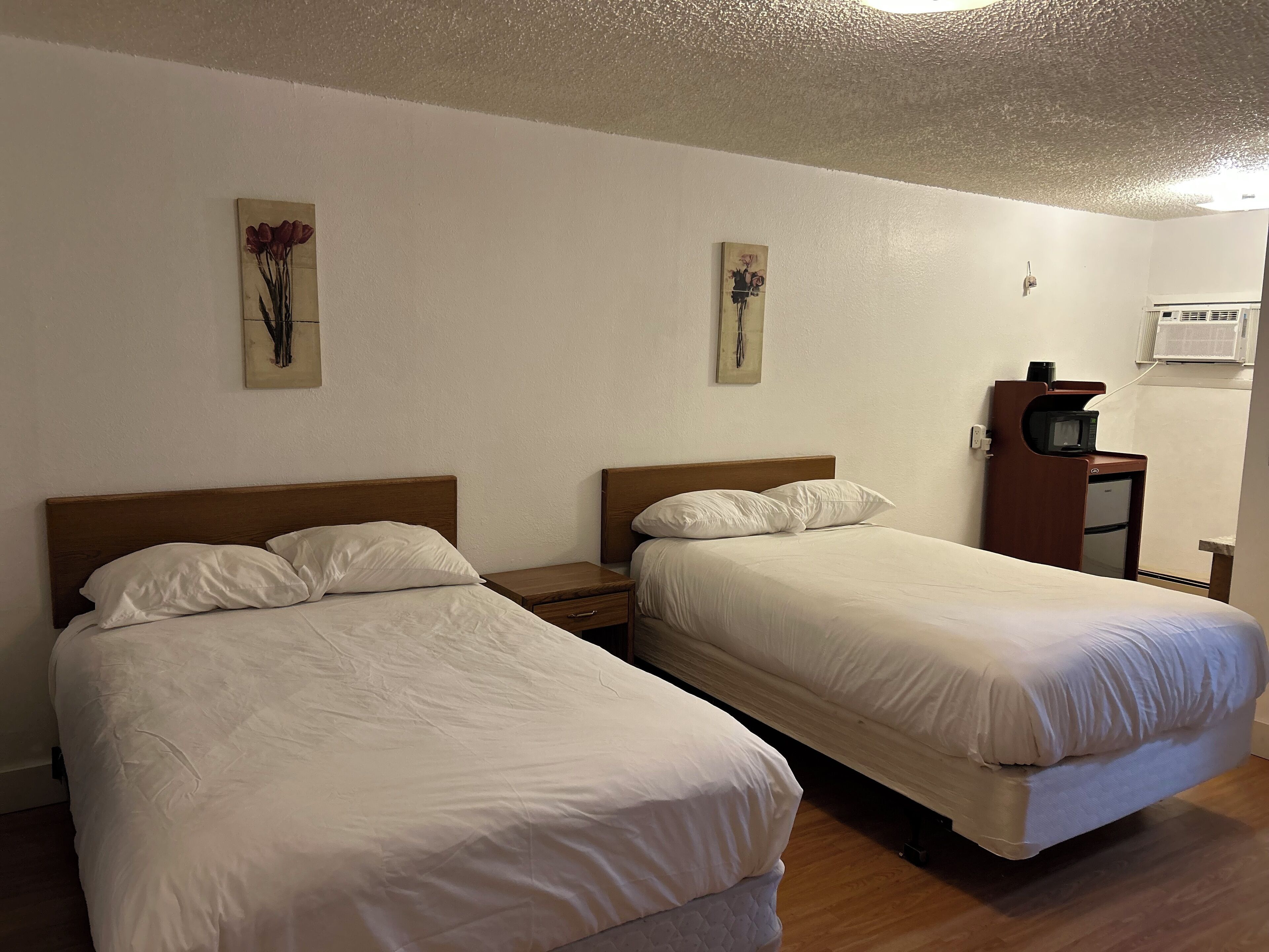 Een hotelkamer met twee eenpersoonsbedden, een houten nachtkastje, een klein houten kastje met een televisie en een wandairconditioning.