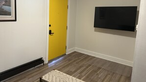 Ein Flur mit einer gelben Tür, einem Wand-Fernseher und einem gerahmten Bild an der Wand.