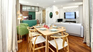 A modern living room with a dining area, a TV mounted on the wall, and a green armchair. - Green Essence Duplex in Faro by Misha s Place (Faro)