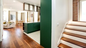 A modern kitchen with green cabinets, a dining area with a white table and chairs, and a staircase with wooden steps. - Green Essence Duplex in Faro by Misha s Place (Faro)